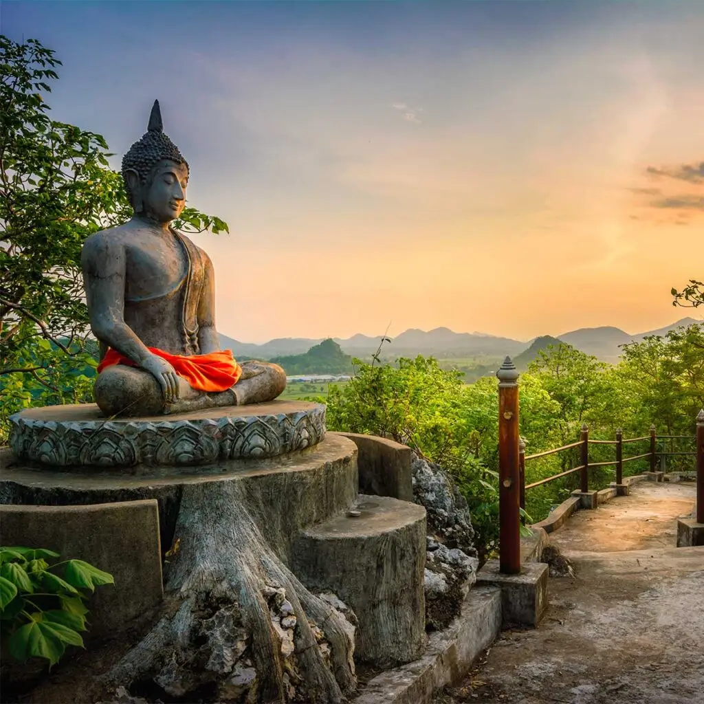 concrete buddha statue on tree stump in garden with trees and mountains in background